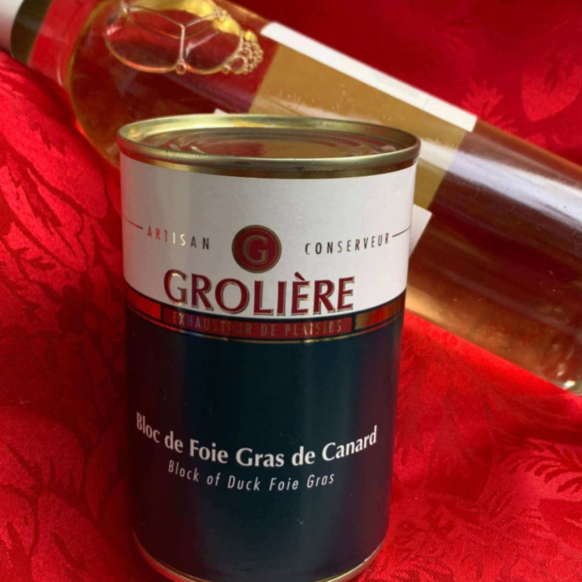 Block of Duck Foie Gras is placed in front of a wine bottle on a red patterned fabric background.