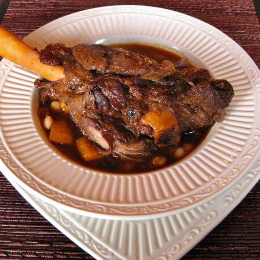 Braised lamb shank with carrots in a white bowl on a wooden surface